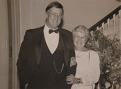 Two people pose together and smile in an archival image, both wearing formal attire.