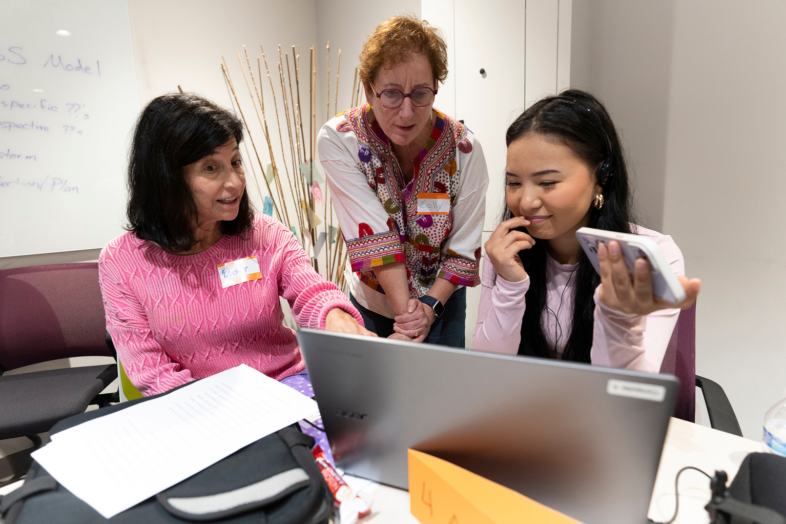 Three people sit around a laptop, looking at the screen and talking.
